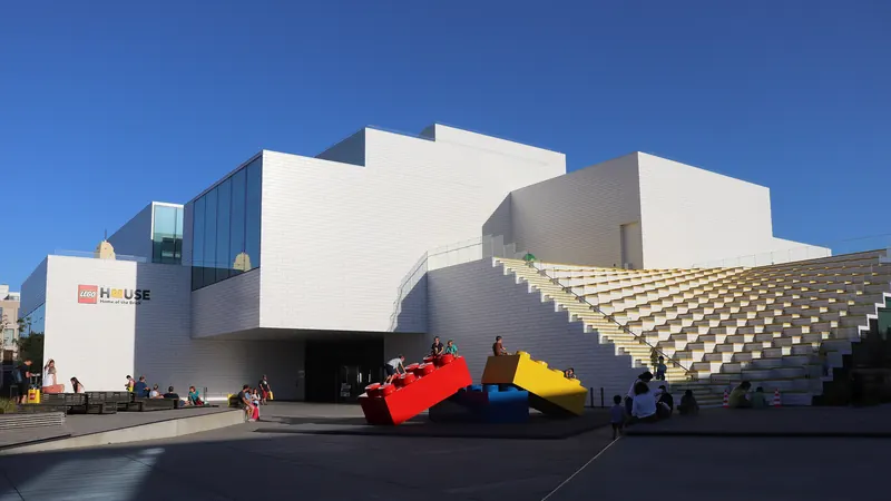 Den hvite, klosseformede bygningen Lego House med store legoklosser foran, under blå himmel