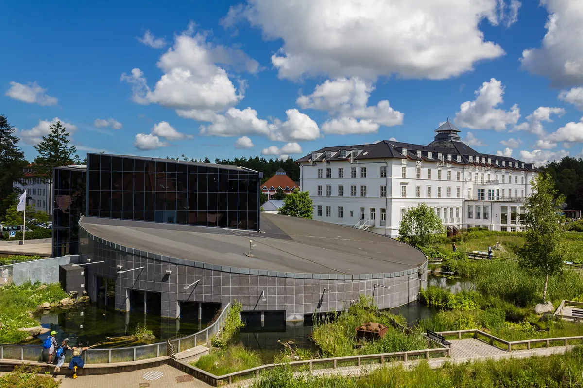 Den runde akvariebygningen AQUA med uteanlegg og et stort hvitt hotell i bakgrunnen