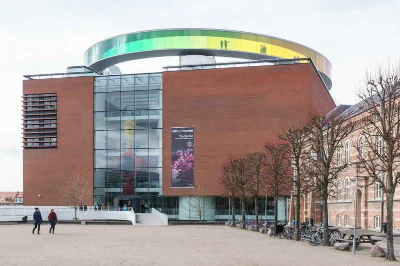 Den røde teglfasaden og glassinngangen til ARoS Aarhus Kunstmuseum med den runde gangbroen på taket