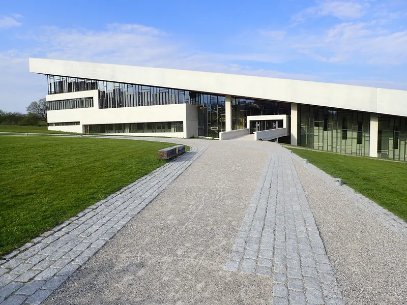 Gangsti mot den hvite, skrå museumsbygningen på Moesgaard med gresstak