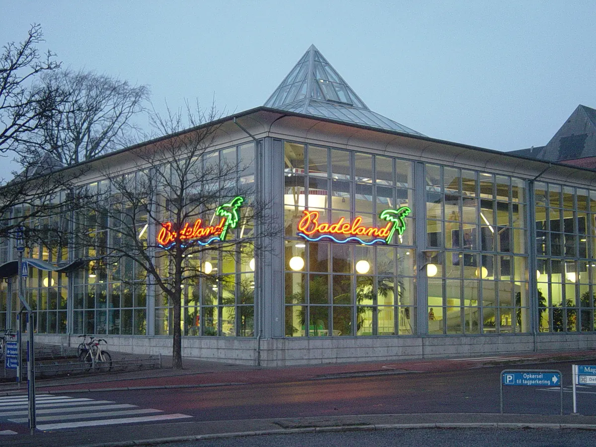 Opplyst glassbygning med palmer i neonskiltet ved inngangen til et badeland i skumringen