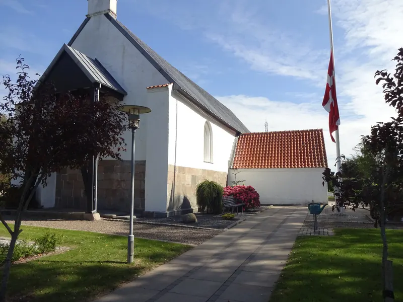 Hvitkalket landsbykirke med rødt tegltak og dansk flagg i Brønderslev