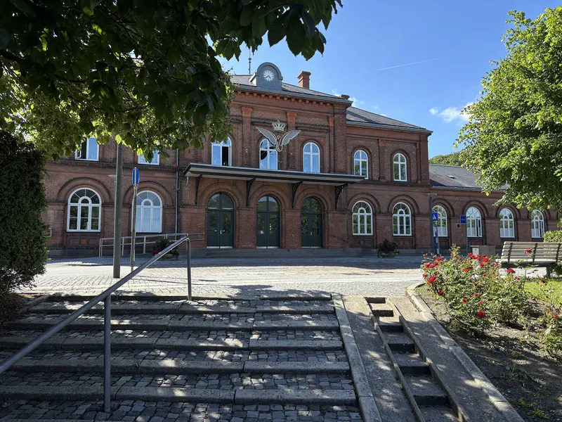 Den røde murstein-stasjonsbygningen i Hobro sett fra en trapp en solrik sommerdag