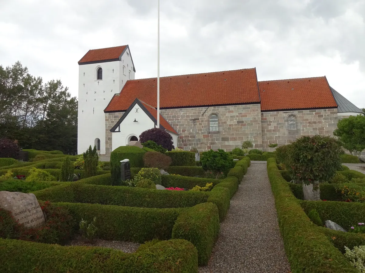 Middelalderkirke med hvitt tårn, rødt tegltak og klippede hekker på kirkegården i Svenstrup