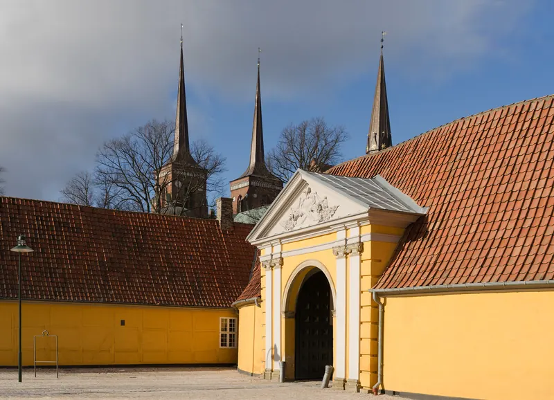 Domkirkens spir rager over gule bygninger og en portal i Roskilde