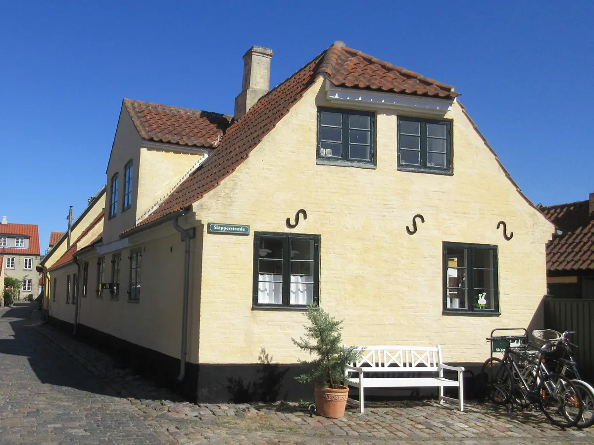 Gult bindingsverkshus med rødt tegltak i en brosteinsgate i gamle Dragør