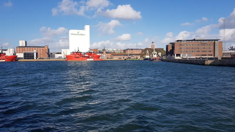 Havnebassenget i Esbjerg med røde skip, siloer og kraftverkspipe under blå himmel