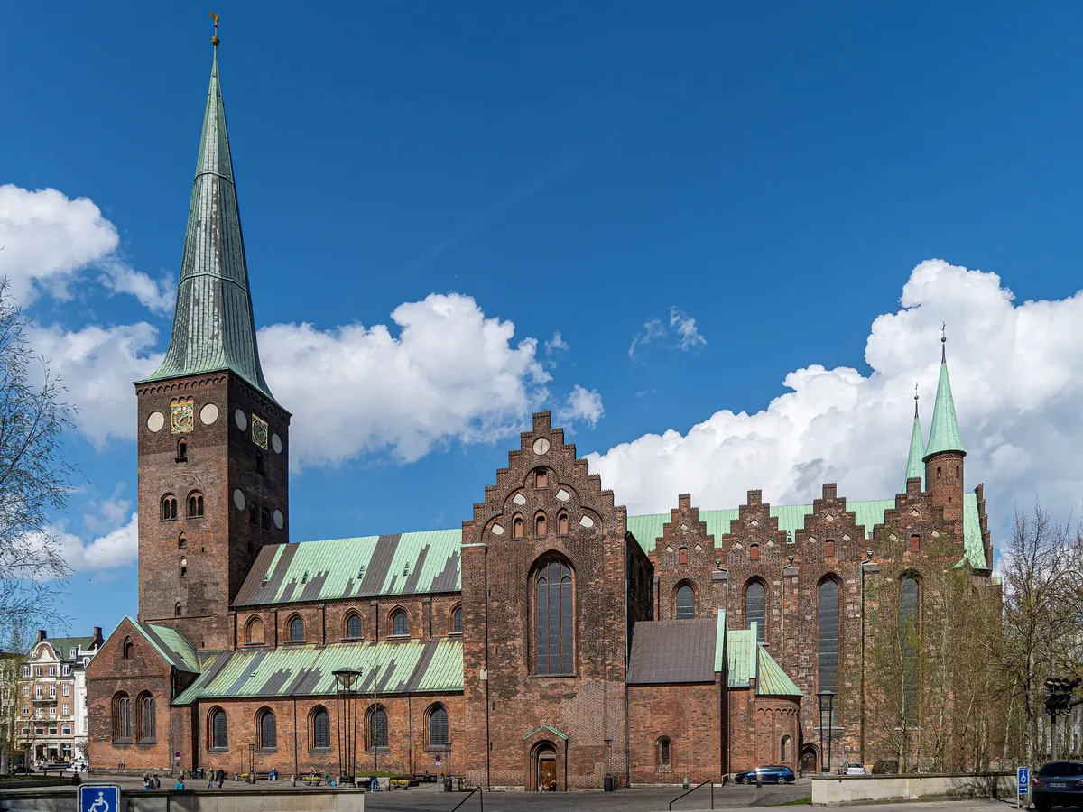Aarhus domkirke i rød tegl med grønt kobbertak og høyt spir under blå himmel