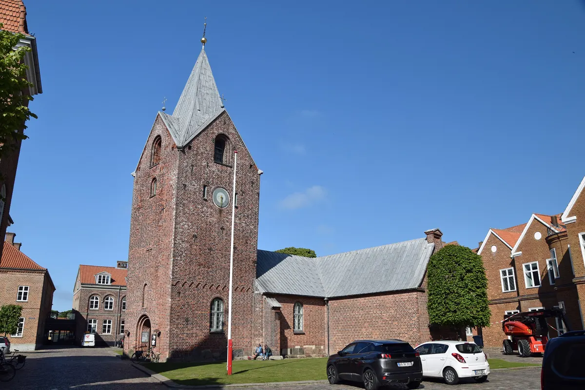 Ringkøbing Kirke med tårn i rød tegl mellom husene i sentrum under blå himmel