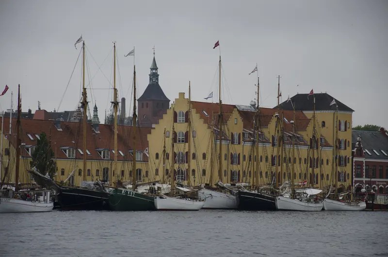 Gamle seilskuter foran gule pakkhus og kirketårn ved havna i Svendborg