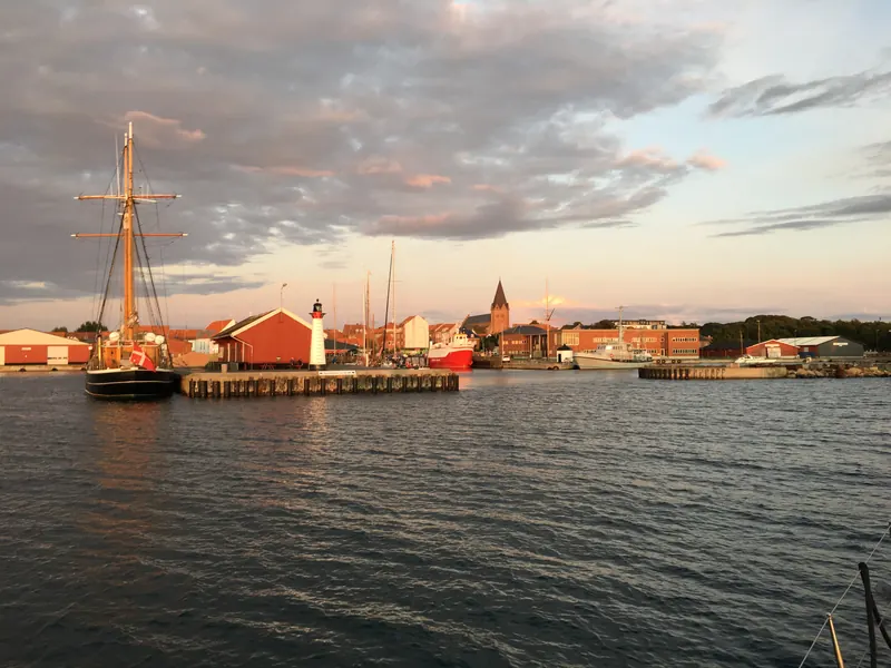 Skonnert ved kaien og byens hustak og kirketårn i kveldssol, sett fra havnen i Assens