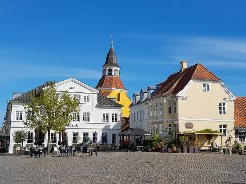 Torvet i Faaborg med klokketårnet og hvite og gule hus under blå himmel