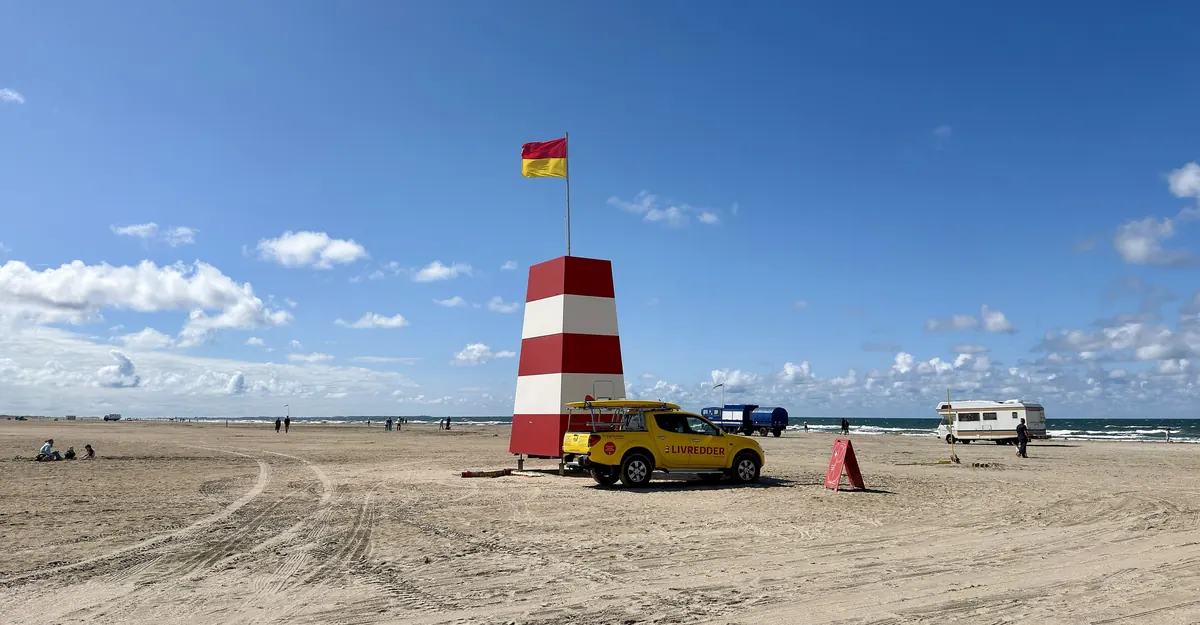 Rød og hvit livredderpost på en bred sandstrand under blå himmel på Rømø