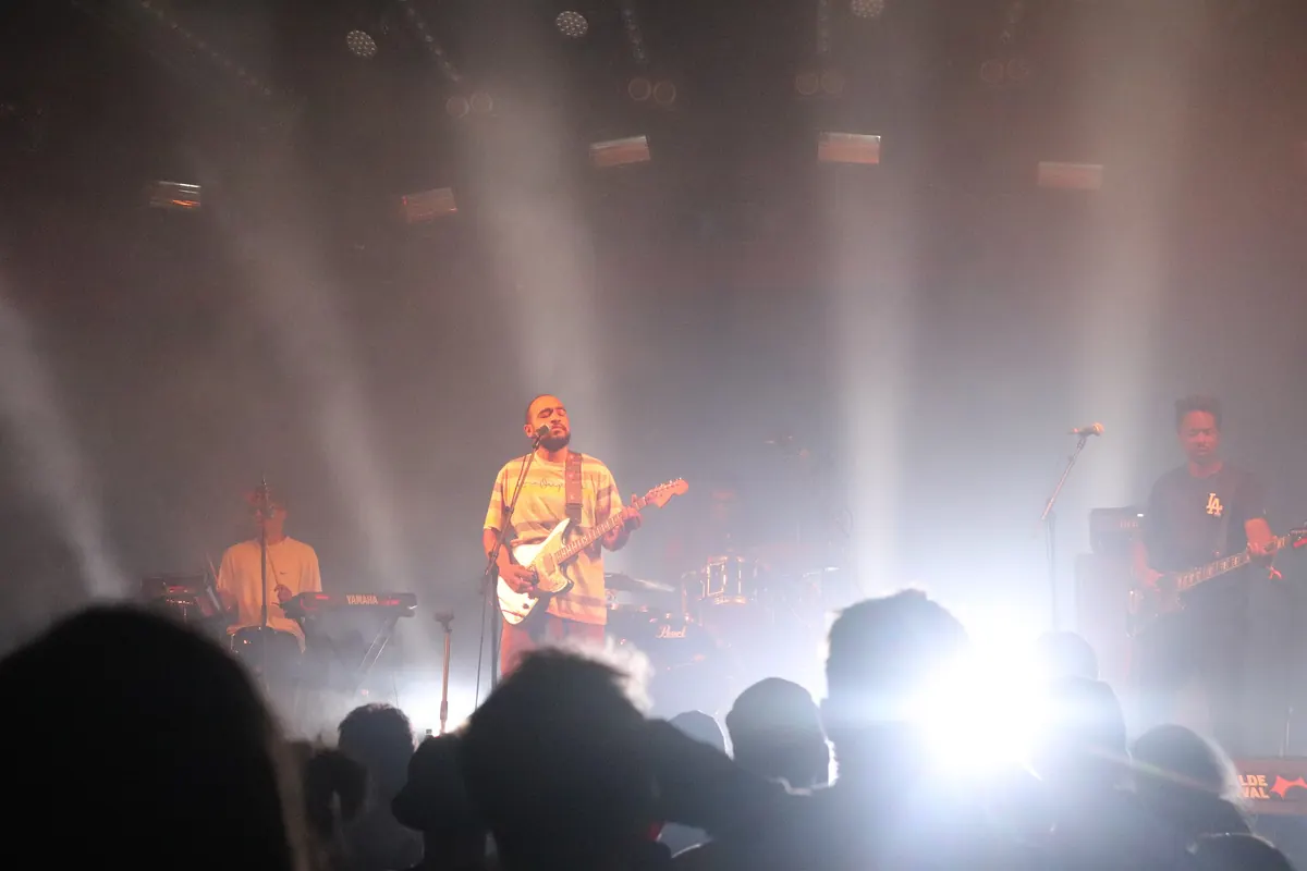 Band på scenen i et konserttelt med lyskastere og publikum i silhuett