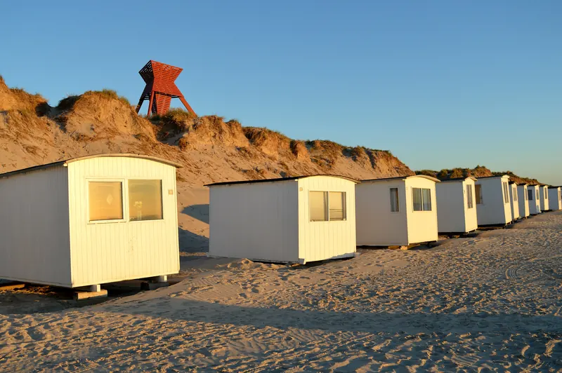 Hvite badehus på sandstranden under klittene i Blokhus i kveldssol