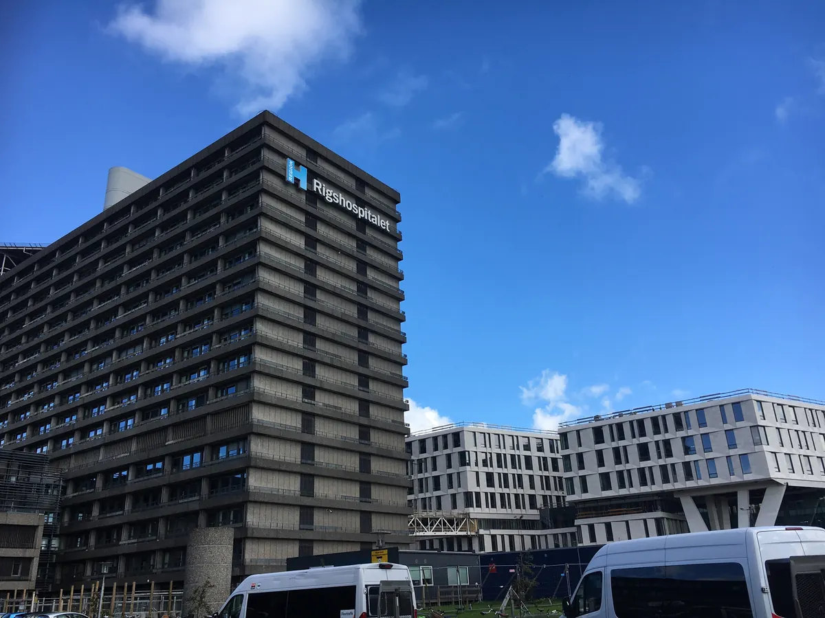 Rigshospitalets høyblokk med logo mot blå himmel i København