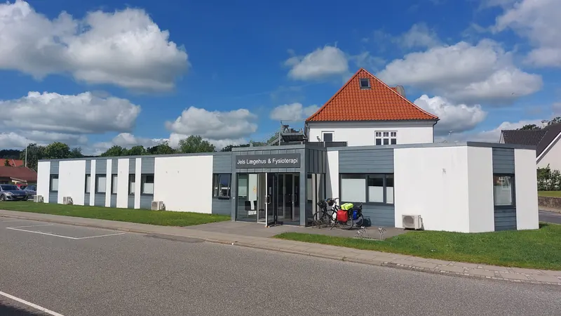 Lavt, hvitt legesenter med rødt tegltak og sykler ved inngangen i en dansk landsby