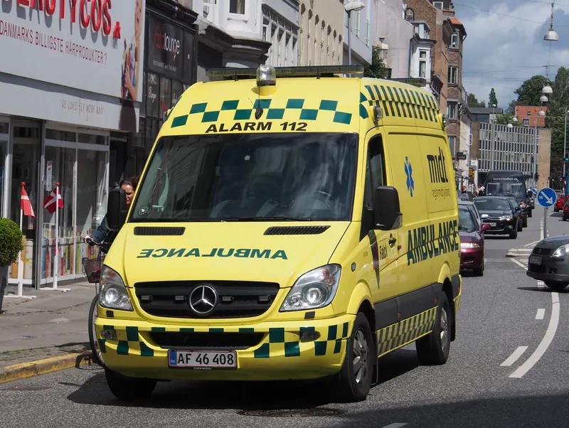 Gul dansk ambulanse med påskriften Alarm 112 i en bygate i Aarhus