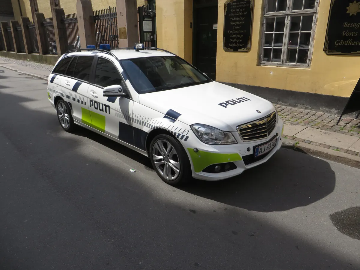 Dansk politibil i hvitt med blå og gulgrønne striper parkert i en gate