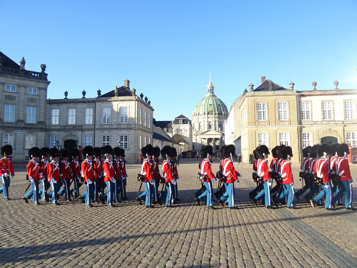 Livgarden i røde gallauniformer marsjerer på slottsplassen på Amalienborg, med Marmorkirkens kuppel bak