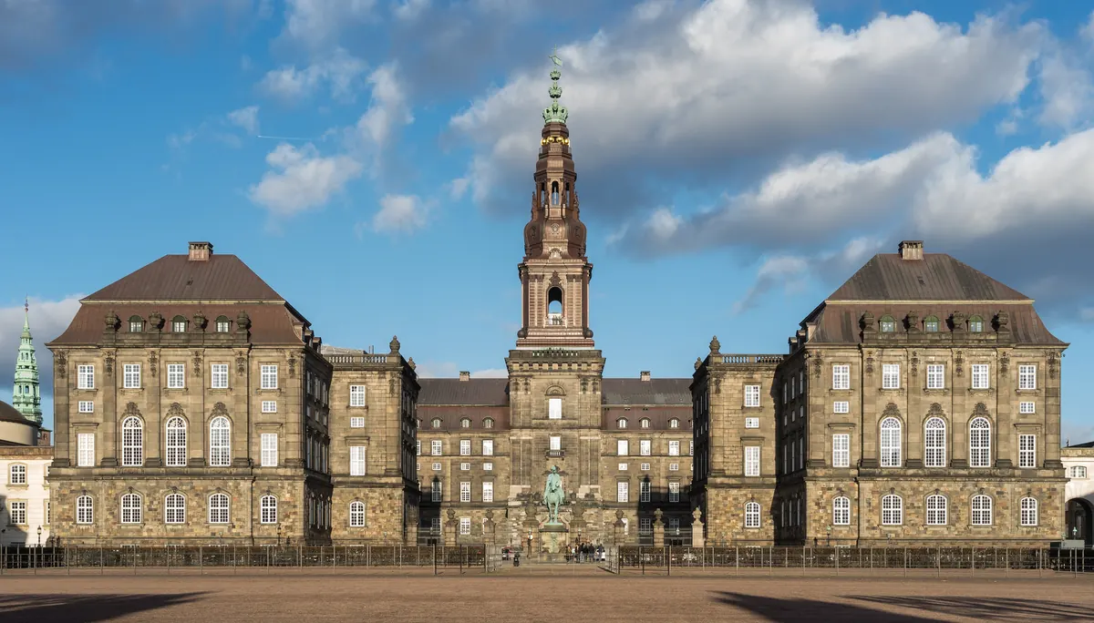 Christiansborg Slot med det høye tårnet midt på fasaden, sett fra ridebaneplassen under blå himmel