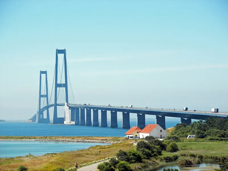 Østbroen over Storebælt med de høye pylonene, sett fra kysten med et hus med rødt tak i forgrunnen