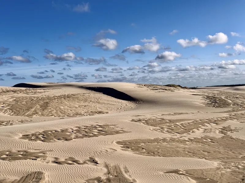 Store, bølgende sanddyner under blå himmel med små hvite skyer