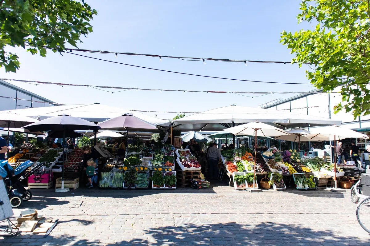 Frukt- og grønnsaksboder under parasoller ved en torghall i København