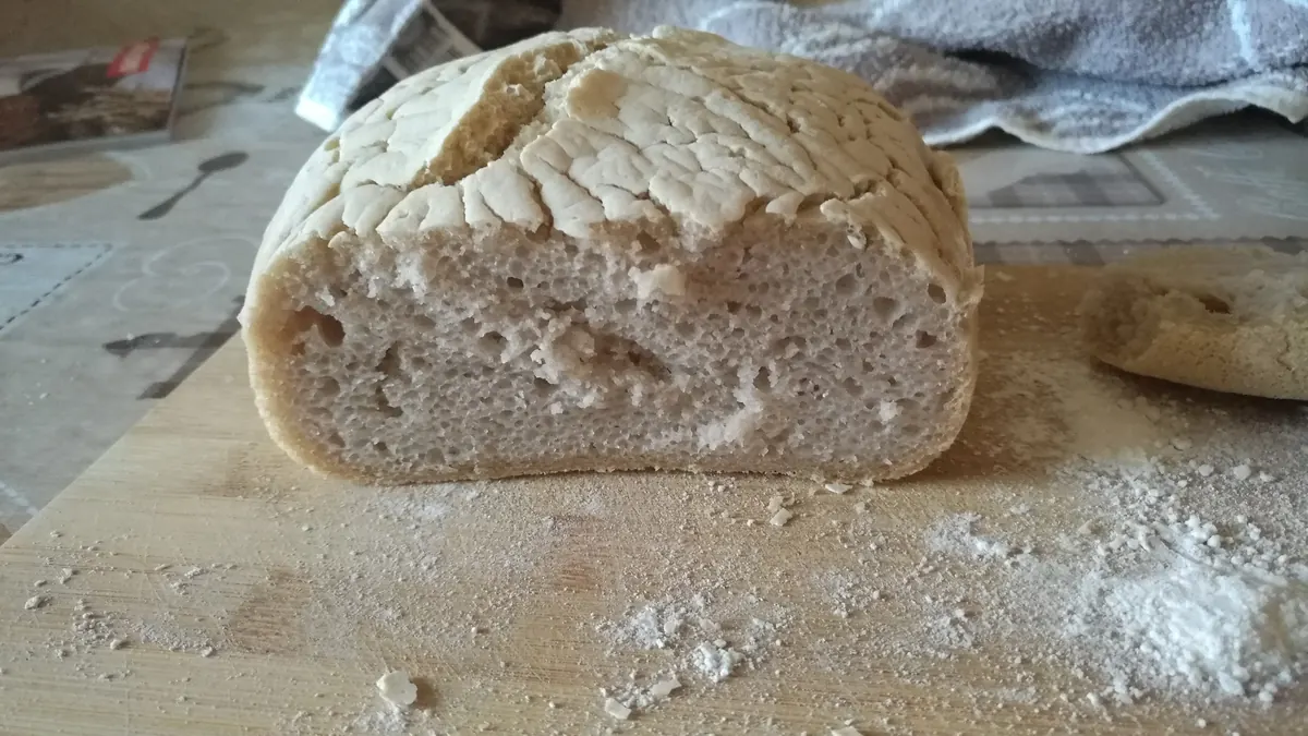 Hjemmebakt glutenfritt brød skåret i to på et melet bakebord
