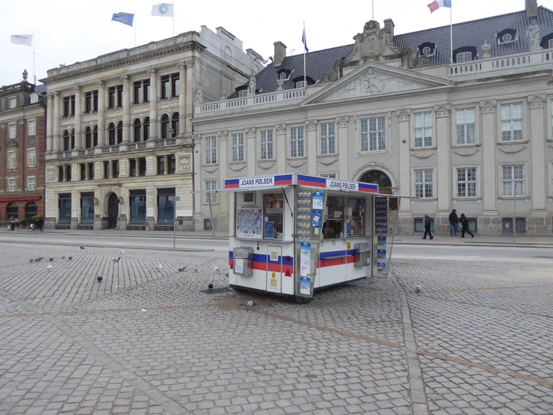 Pølsevogn på en brolagt plass foran klassiske bygninger i København