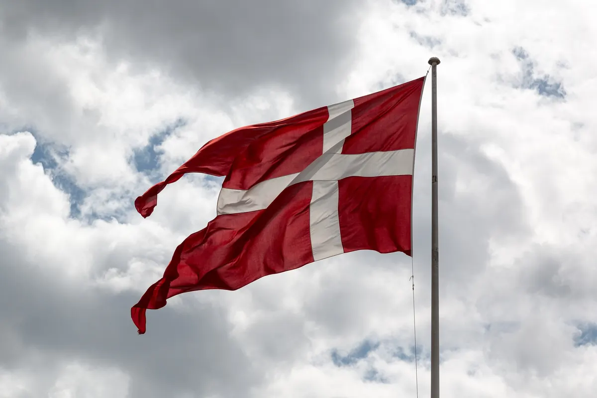 Det danske flagget Dannebrog vaier i vinden mot en skyet himmel
