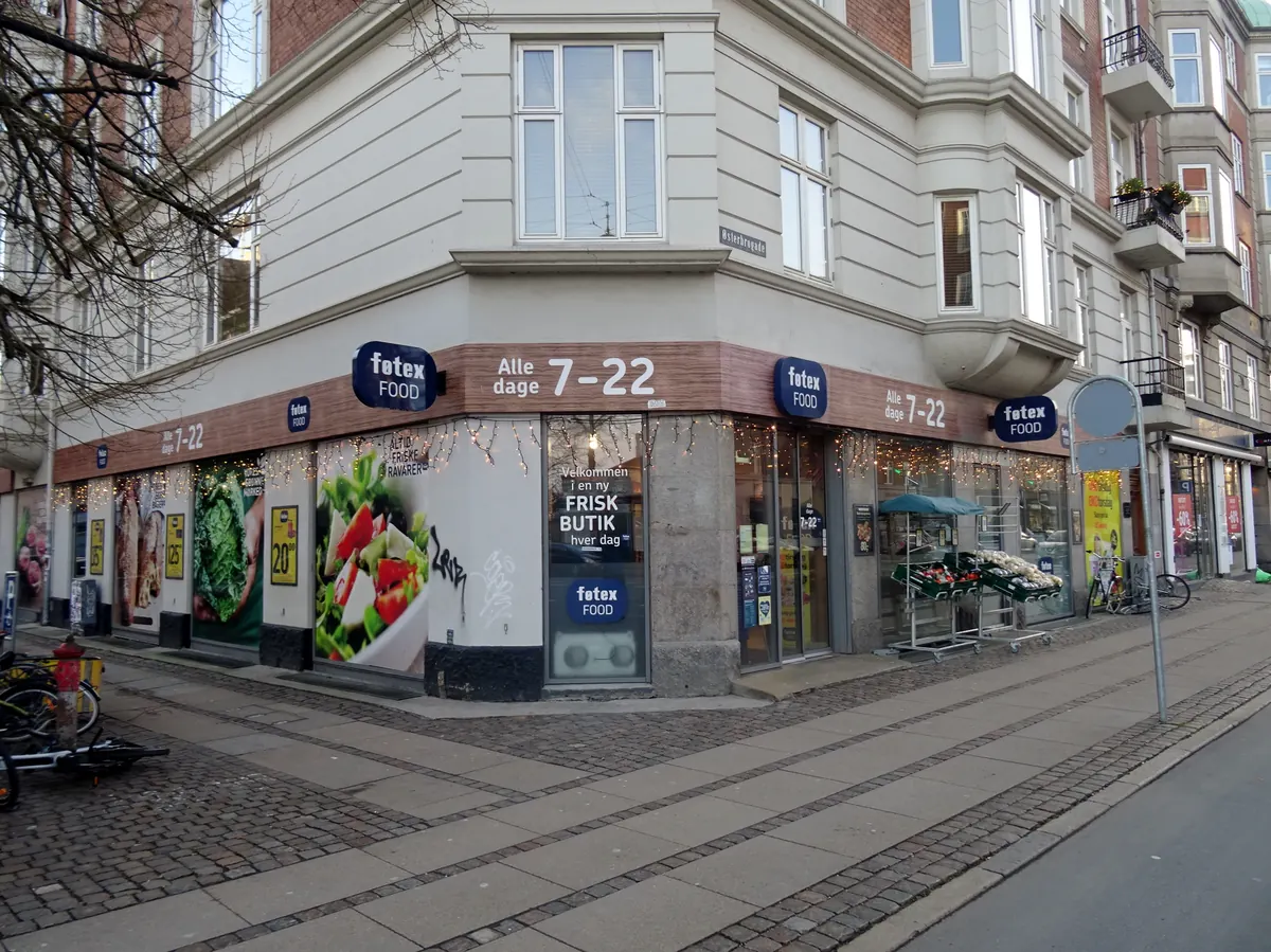 Hjørnebutikk i en bygate med skilt som viser åpent alle dager 7–22