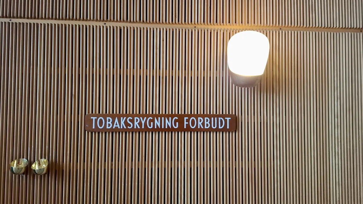 Skilt med teksten «Tobaksrygning forbudt» på en vegg av trepaneler med lampe