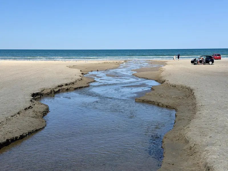 Bekk som renner ut i havet over en bred sandstrand ved Blokhus en solrik dag