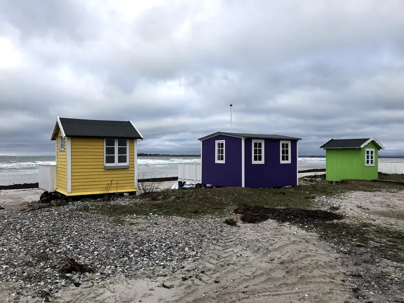 Tre fargerike badehus i gult, lilla og grønt ved stranden i Ærøskøbing