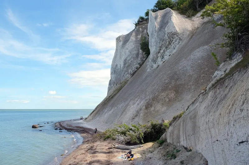 Hvite krittklipper som stuper ned mot en smal strand og blått hav ved Møns Klint