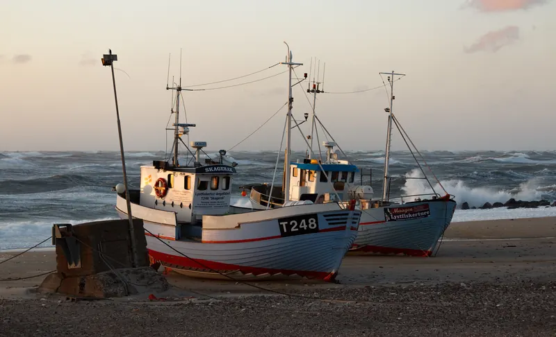 Fiskebåter trukket opp på stranden i Nørre Vorupør i kveldssol med brenninger bak