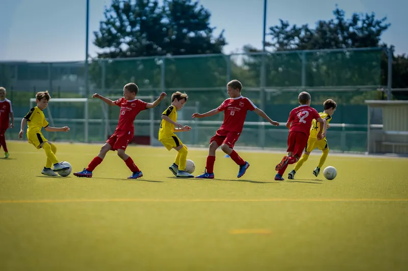 Barn i røde og gule drakter spiller fotball på en kunstgressbane